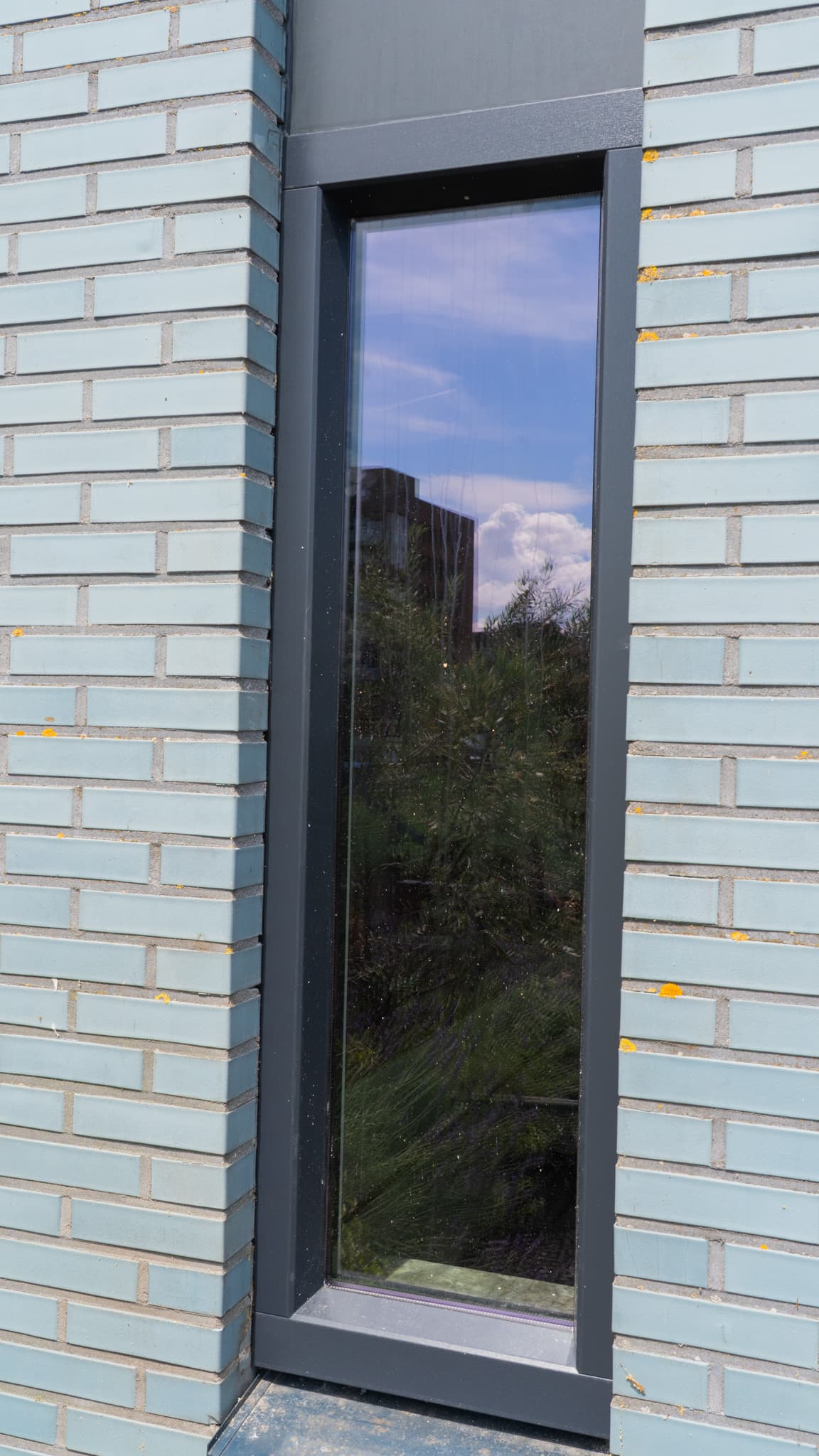 Smal antraciet aluminium kozijn in lichtblauwe baksteengevel Den Haag