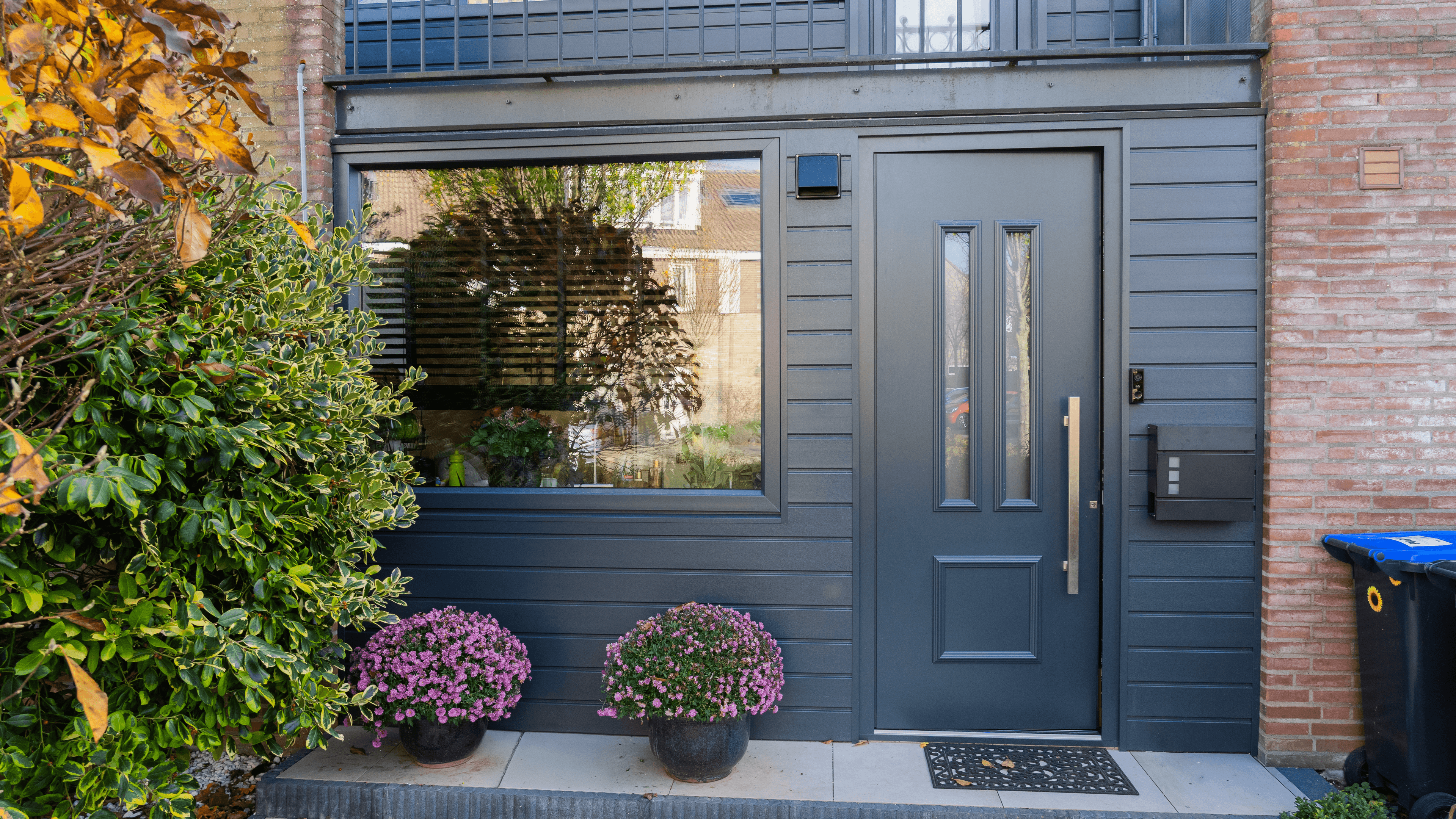 Moderne antraciete aluminium voordeur met zijraam en groene beplanting
