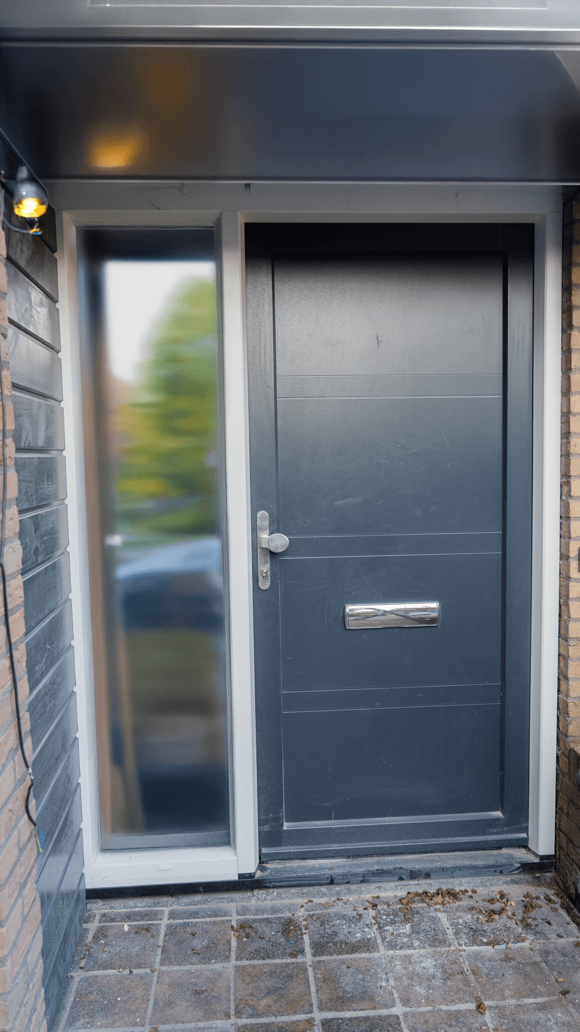 Antraciete aluminium voordeur met zijlicht in donkere bakstenen gevel