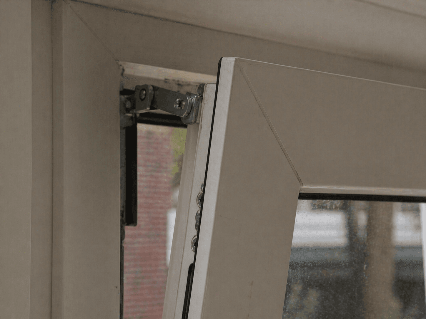 Beslag en schaar van een draaikiepraam in de bovenhoek van het kozijn